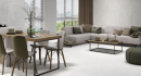 Salon połączony z kuchnią z płytkami podłogowymi imitującymi beton, antypoślizgowymi Cifre Acron Pearl Mate Antislip 90x90, z białą sofą z poduszkami, z niskim stolikiem kawowym, stołem z drewnianym blatem,  krzesłami, żaluzjami i lamelami.