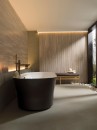 Łazienka z betonową podłogą, czarną wanną wolnostojącą oraz płytkami ściennymi imitujacymi trawertyn Porcelanosa Canal Roma Noce