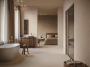 Łazienka połączona z sypialnią z białą wanną wolnostojącą i płytkami imitującymi kamień Porcelanosa Coral Caliza i Deco Coral Caliza