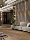 Salon z szarą sofą wypoczynkową, szklanymi podświetlanymi witrynami, ozdobną ścianą i brązowymi drewnopodobnymi płytkami podłogowymi Porcelanosa Gent Roble Matt