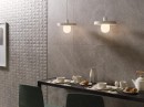 Aranżacja wnętrza z czarnym blatem przy ścianie, wiszącymi lampami oraz szarymi płytkami ściennymi imitującymi kamień Porcelanosa Mystic Grey L Matt