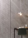 Aranżacja wnętrza z czarnym blatem przy ścianie, wiszącymi lampami oraz szarymi płytkami ściennymi imitującymi kamień Porcelanosa Mystic Grey L Matt