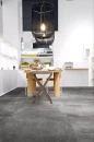 Nowoczesna jadalnia z drewnianym stołem, lampami wiszącymi, białymi szafkami i płytkami podłogowymi imitującymi beton Florim Architectural Design Rawtech Raw-Coal Naturale
