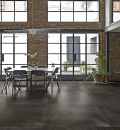 Jadalnia w stylu industrialnym z dużymi oknami, stołem i czarnymi krzesłami, wiszącą lampą i płytkami podłogowymi imitującymi metal Florim Architectural Design Flowtech Burnished Naturale