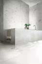 Nowoczesna jasna łazienka z wanną, srebrną baterią wannową, ozdobną ścianą i płytkami imitującymi marmur Florim Contemporary Design Timeless Calacatta
