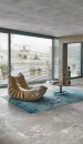 Salon w stylu loftowym z dużymi oknami, fotelem, turkusowym dywanem i podłogą imitującą kamień Florim Creative Design Onyx&More White Porphyry