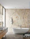 Łazienka z białą wanną wolnostojącą, dużym oknem, białą umywalką nablatową i płytkami na ścianie imitującymi kamień Florim Creative Design Onyx&More Golden Onyx
