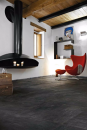 Aranżacja wnętrza z kominkiem, czerwonym fotelem, drewnianymi deskami sufitowymi i podłogą imitującą kamień Florim Luxury Design Ardoise Noir