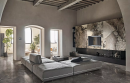 Nowoczesny salon w stylu glamour z dużą kanapą wypoczynkową, ozdobną ścianą z telewizorem oraz płytkami podłogowymi imitującymi marmur Florim Luxury Design Heritage Luxe Heritage Brown