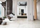 Nowoczesne wnętrze z białymi ścianami i filarami, czarnymi schodami i płytkami podłogowymi imitującymi marmur Florim Luxury Design I Classici Calacatta Gold