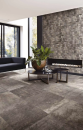 Salon z ozdobną ścianą, stolikiem, czarną kanapą, dużymi oknami tarasowymi i podłogą imitującą kamień Florim Luxury Design La Roche Mud