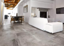 Duży salon z jasną kanapą, połączony z jadalnią ze stołem i krzesłami oraz podłoga imitującą kamień Florim Luxury Design La Roche Grey