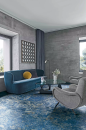 Salon z dużymi oknami, betonową ścianą, niebieską kanapą, fotelami i płytkami podłogowymi imitującymi marmur Florim Luxury Design Les Bijoux Sodalite Bleu