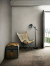Aranżacja pomieszczenia z fotelem, szarymi ścianami przypominającymi beton oraz płytkami podłogowymi imitującymi kamień Florim Luxury Design Matières Brun
