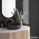 Płytki ścienne Equipe Island Black 6,5x20 wyłożone na ścianie z półokrągłym lustrem, szafką umywalkową oraz umywalką podwieszaną ze złotą armaturą