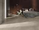 Sypialnia z łóżkiem, stolikiem nocnym, lampką, krzesłem, betonową ścianą i płytkami podłogowymi imitującymi kamień Leonardo Ceramica 65 Parallelo .65PRL 75B