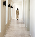 Długi korytarz z oknami, czarnymi kinkietami i płytkami podłogowymi imitującymi marmur Leonardo Ceramica One DOR NU