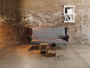 Aranżacja wnętrza w stylu industrialnym ze ścianą z cegieł, kanapą, stojąca lampą oraz płytkami podłogowymi imitującymi beton Leonardo Ceramica WATERFRONT 90CP