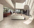 Salon połączony z kuchnią w stylu loftowym z białą kanapą, betonowymi ścianami i płytkami podłogowymi imitującymi beton Alfalux Kompakt Beige