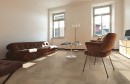Salon z brązową kanapą, fotelem, stolikiem kawowym, stojącą lampą i płytkami podłogowymi imitującymi beton Alfalux Materika Moka