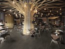 Nowoczesne wnętrze restauracji z ozdobnym filarem z lampami, brązowymi stolikami i krzesłami oraz czarnymi płytkami podłogowymi imitującymi beton w naturalnym wykończeniu Alfalux Materika Moka
