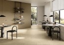 Kawiarnia z płytkami Fioranese Autentica Light Beige Naturale 60,2x60,4 AU361R wyłożonymi na podłodze, duże okna, czarne stoliki na jednej nodze