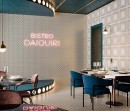 Wnętrze bistro ze stolikami, niebieskimi fotelami, neonowym napisem i dekoracyjnymi płytkami na ścianie Aparici Art-Deco White Negroni oraz na ścianie i podłodze ze wzorem w pawie pióra Aparici Art-Deco White Daiquiri