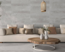 Salon z jasną kanapą wypoczynkową, szarymi płytkami podłogowymi Colorker Solange Grey oraz dekoracyjnymi na ścianie, imitującymi kamień, Colorker Solange Grey Decor