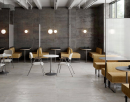 Wnętrze restauracji w stylu industrialnym, ze stolikami i krzesełkami, lożami barowymi, szarą podłogą Colorker Sonar Silver i czarnymi płytkami na ścianie imitującymi metal Colorker Sonar Iron