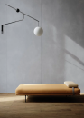 Pomieszczenie z drewniana podłogą, minimalistyczną leżanką, lampą oraz płytkami na ścianie w kolorze szarym, imitującymi beton, w matowym wykończeniu Paradyż Ceramika Architeq Grey Mat