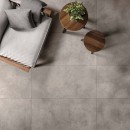 Fotel wypoczynkowy, małe drewniane stoliki kawowe oraz szare płytki podłogowe imitujące beton, matowe Flaviker Hyper Grey Naturale