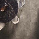 Czarny marmurowy stół z jasnymi krzesłami, brązowe płytki podłogowe imitujące beton, matowe Flaviker Hyper Taupe Naturale