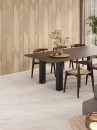 Płytka ścienna imitujące drewniane lamele hiszpańskiego producenta Porcelanosa Gent Arrow 3D Arce 59,6x150 wyłożone na ścianie jadalni. Kontrastujący ciemny, drewniany stół stojący na podłodze z wyłożonymi płytkami z szarego kamienia.