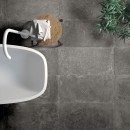 Łazienka z białą wanną wolnostojącą, białą baterią i grafitowymi płytkami na podłodze imitującymi beton Flaviker Backstage Graphite Naturale