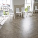 Salon z białymi krzesłami i dużymi oknami oraz szarymi marmurowymi płytkami Marazzi Allmarble Tafu