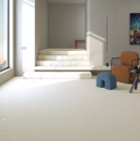 Wnętrze holu z dużym oknem, brązowym fotelem, schodami i białymi płytkami podłogowymi imitującymi beton z efektem mieszania farby Arcana Spuma-R Panna