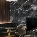 Salon wyłożony czarnymi, matowymi płytkami marmurowymi Marazzi Allmarble Calacatta Black Natural MELJ 60x120 cm, z czarną sofą stojącą niedaleko komina oraz okrągłym stolikiem wraz z szarym krzesłem