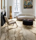 Salon wyłożony na podłodze matowymi płytkami marmurowymi, bezowymi Marazzi Allmarble Calacatta Vena Vecchia MF6K 60x120 cm, w centrum którego stoi mały czarny stolik kawowy, obok którego ustawiona jest biała sofa oraz biały fotel