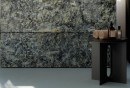 Ściana pokryta matowymi płytkami marmurowymi w niebiesko-szarym kolorze Marazzi Allmarble Quarzo Bluegrey 60x120 cm MF6M, przy której stoi czarny stolik