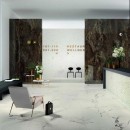 Hol wyłożony białymi płytkami marmurowymi z czarną żyłą, Marazzi Allmarble Statuario MMGT 60x120 cm z recepcją, czarną podłużną pufą oraz szarym krzesełkiem w centrum