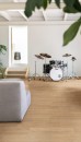 Salon wyłożony płytkami drewnopodobnymi Marazzi Alma Miele 20x120 cm MFDC , ze stojącą w rogu perkusją i szarą sofą w centrum