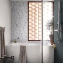 Łazienka z białymi patchworkowymi płytkami na wprost, matowymi płytkami imitującymi beton w niebieskim kolorze Marazzi Cementum Indigo po prawej stronie oraz dużą białą wanną, na której wisi ręcznik i stoi drzewko w doniczce