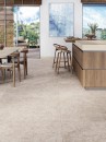 Otwarta kuchnia z jadalnią, drewnianą wyspą, stołem, krzesłami i ciemnobeżowymi płytkami na podłodze imitującymi beton Porcelanosa Cancun Stone L