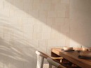 Jadalnia z drewnianym stołem i kremowymi pytkami ściennymi imitującymi beton, matowa, strukturalna powierzchnia Porcelanosa Block Cancun Sand