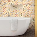 Ściana wyłożona matowymi, dekoracyjnymi płytkami ściennymi multikolorowymi, Marazzi Cloud Decoro Mandala Cream 20x50 cm, przed którą stoi biała wanna