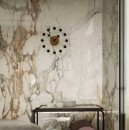 Ściana wyłożona połyskującymi beżowymi płytkami imitującymi marmur, Marazzi Grande Marble Look Calacatta Vena Vecchia Lux MEMV 120x120 cm, z designerskim zegarem w centrum