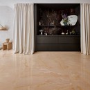 Salon z beżowymi płytkami podłogowymi oraz czarną meblościanką ozdobioną połyskującymi czarnymi płytkami imitującymi marmur na ścianie, Marazzi Grande Marble Look Onice Nero Lux