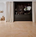 Salon z jasnymi zasłonami i błyszczącą podłogą z płytek Marazzi, w głębi widać meble na tle ściany wykończonej czarną płytką Marazzi Grande Marble Look Onice Nero Lux