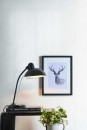 Ściana w pokoju wyłożona płytkami Marazzi Grande Solid Color Look White Lux, czarna lampa i grafika z jeleniem stanowią dekoracyjne akcenty na tle białej ściany