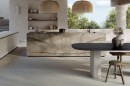 Aranżacja kuchni z wykorzystaniem płytek Marazzi Grande Stone Look Silver Root Naturale na wyspie, z drewnianym stołem i rattanowymi lampami stanowiącymi eleganckie akcenty na tle naturalnego kamienia